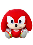 A plush toy of the character Knuckles from Sonic, featuring his signature red body, cream-colored snout and hands, and gray feet with red, yellow, and green accents, set against a plain white background.