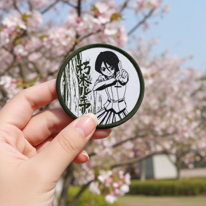 Hand holding a circular patch with an anime character against a cherry blossom background