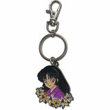An anime keychain charm featuring a character with black hair and a purple top surrounded by white and yellow flowers, attached to a silver metal split ring and lobster clasp on a white background.