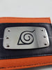 Close-up of an orange and black fabric headband featuring a silver metal plate with an engraved black Naruto-style leaf symbol.